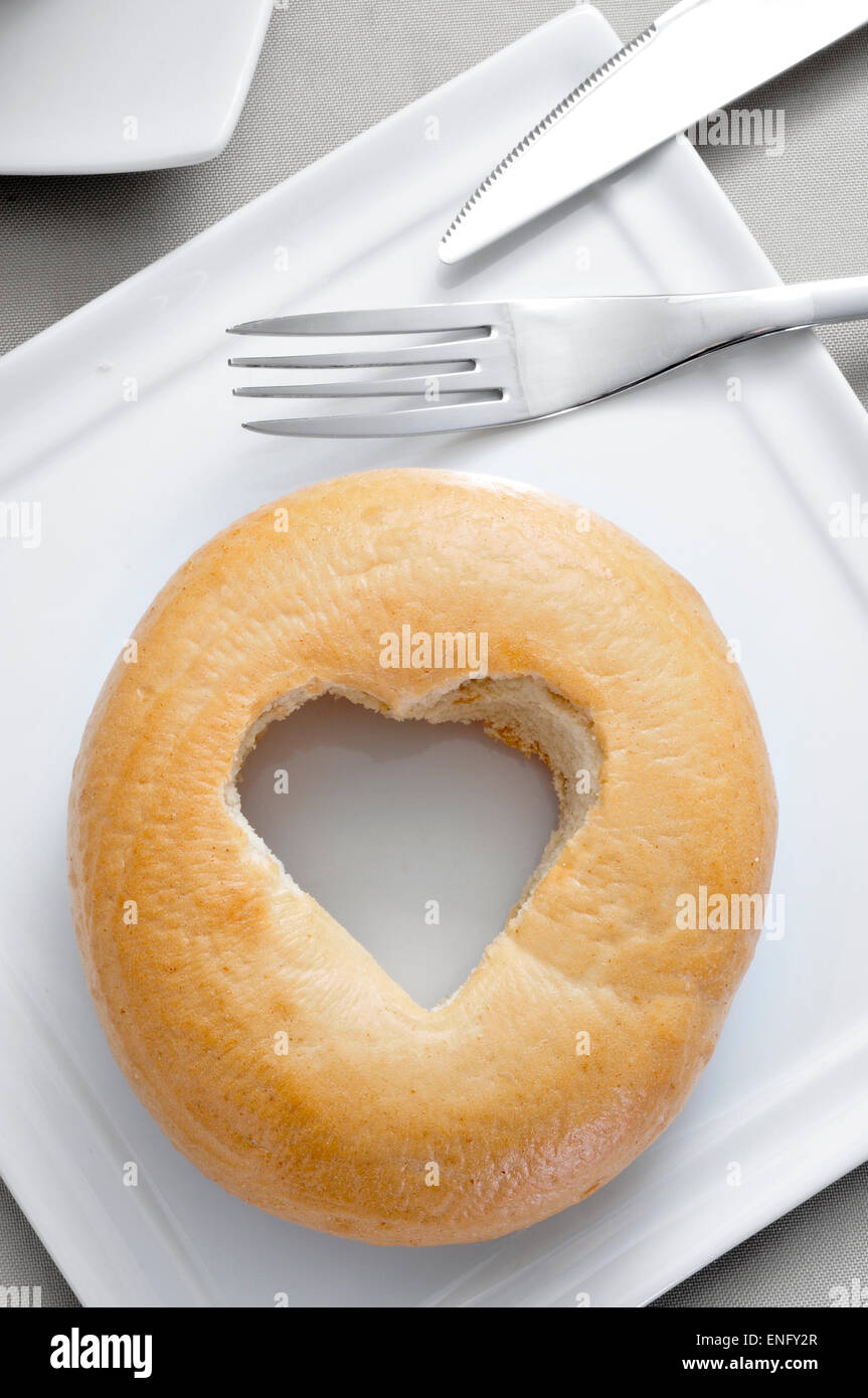 eine Platte mit einem Flugzeug-Bagel mit einem herzförmigen Loch auf einem gedeckten Tisch Stockfoto