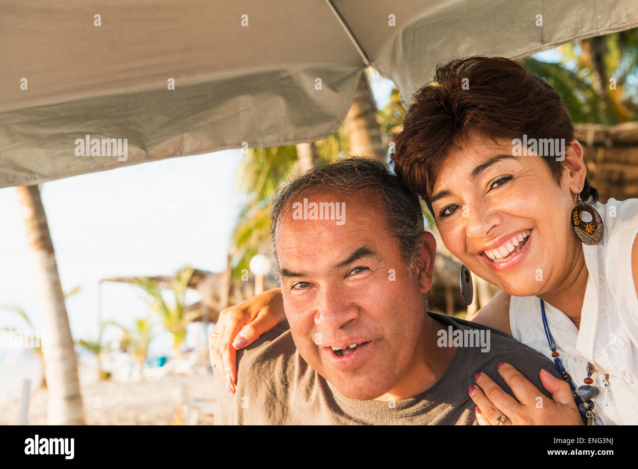Hispanische paar lächelnd unter Sonnenschirm am Strand Stockfoto