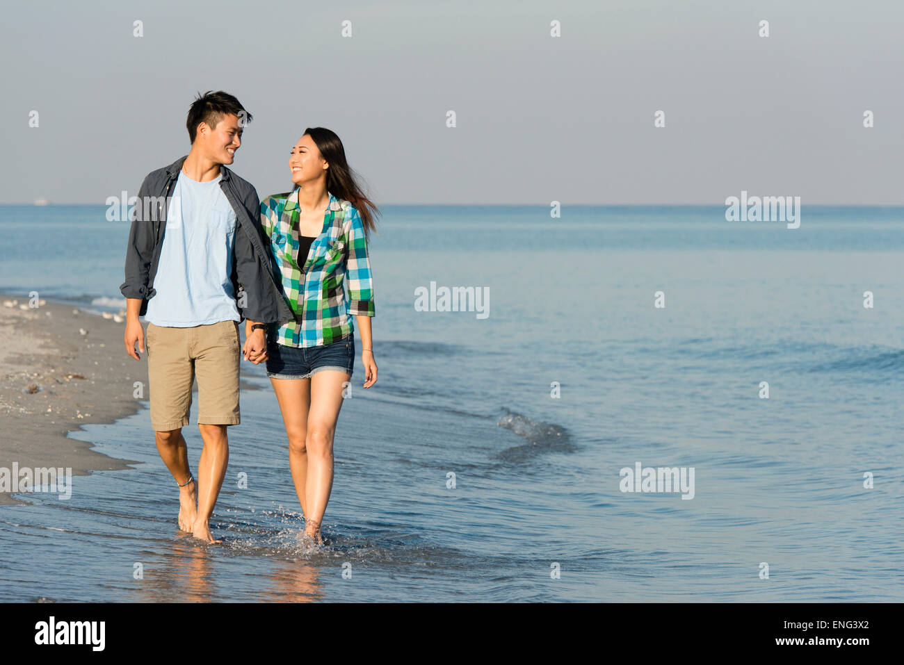 Koreanische Paare, die in Wellen am Strand Stockfoto