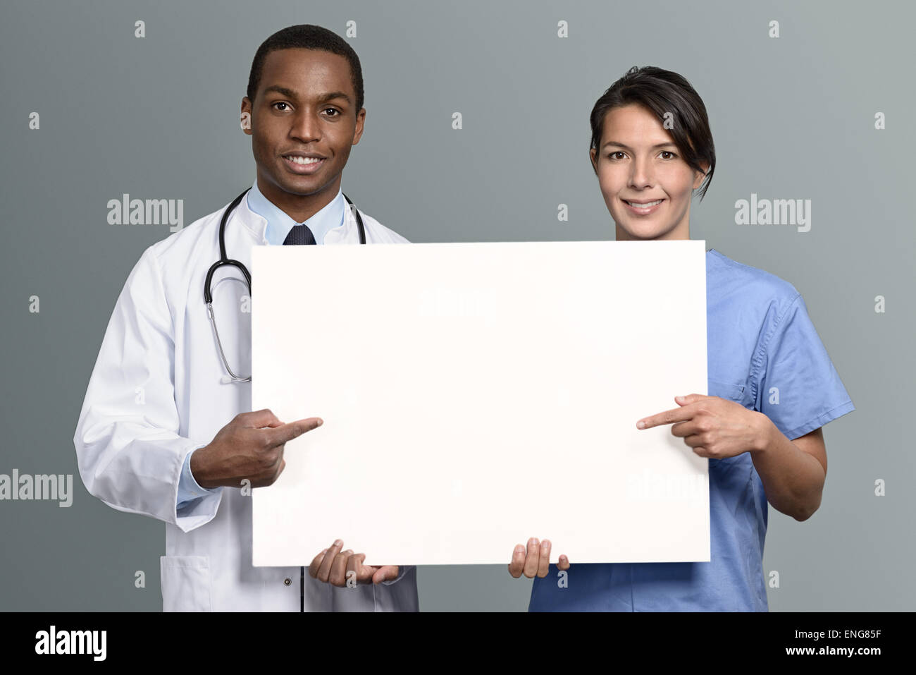 Multiethnische Ärzteteam ein afrikanischer Arzt in einem Kittel und Stethoskop und einer Krankenschwester in Peelings mit einem leeren weißen Schild Stockfoto