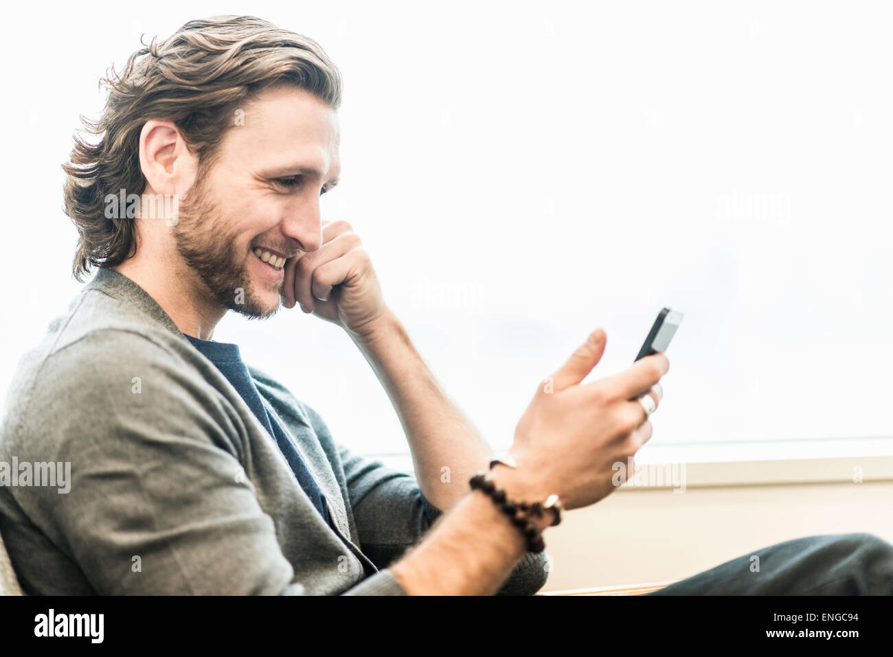 Ein bärtiger Mann sitzt lächelnd und überprüft seine Telefon. Stockfoto