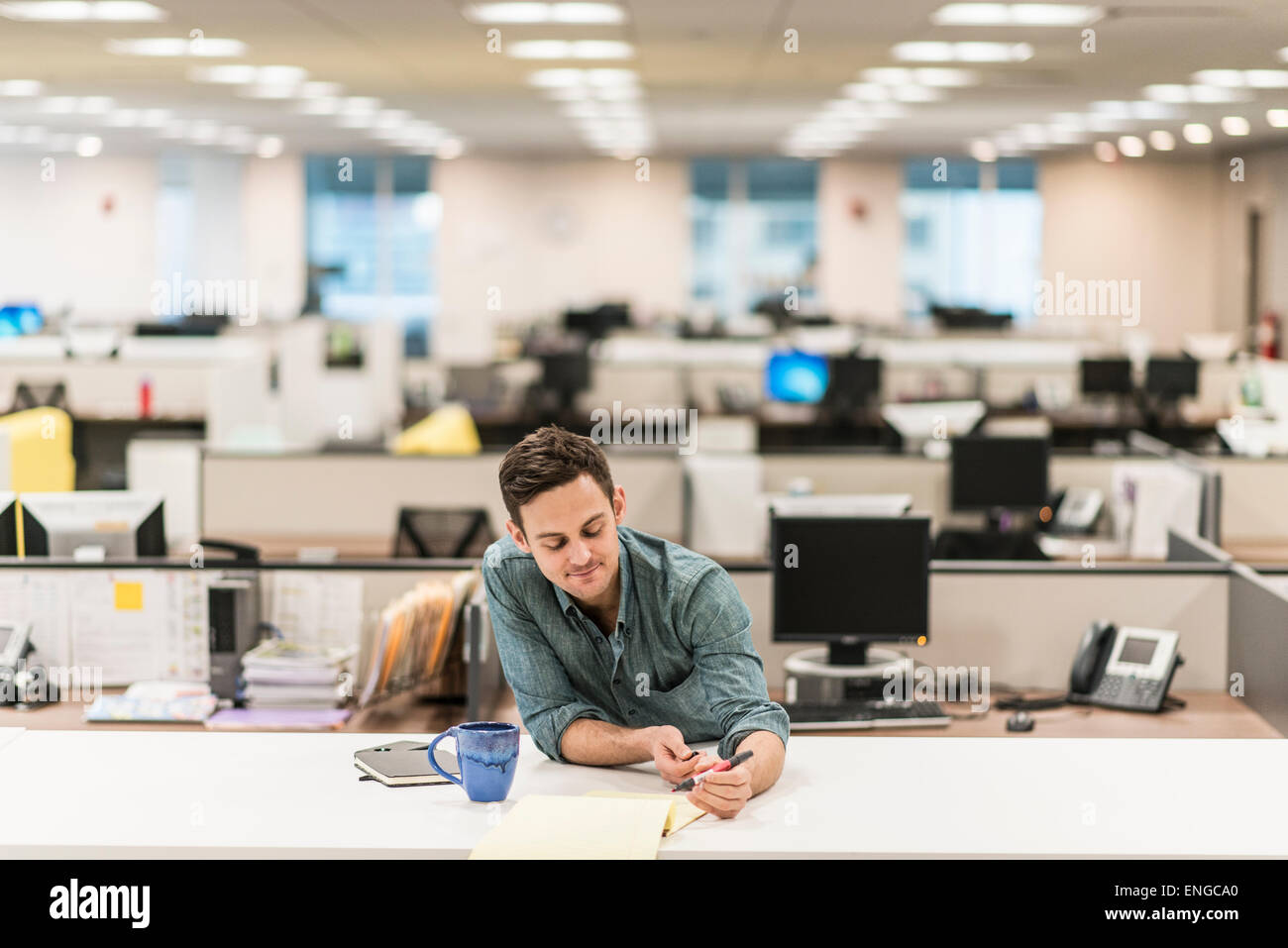 Ein junger Mann sitzt an einem Schreibtisch in einem Büro einen Stift halten. Stockfoto
