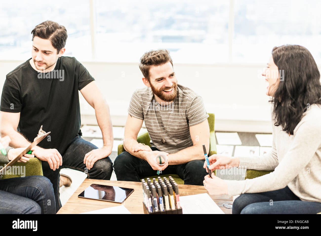 Vier Personen sitzen an einem Tisch mit Kollegen bei einer Planungsbesprechung holding Farbstiften und arbeiten auf Papier und Tabletten. Stockfoto