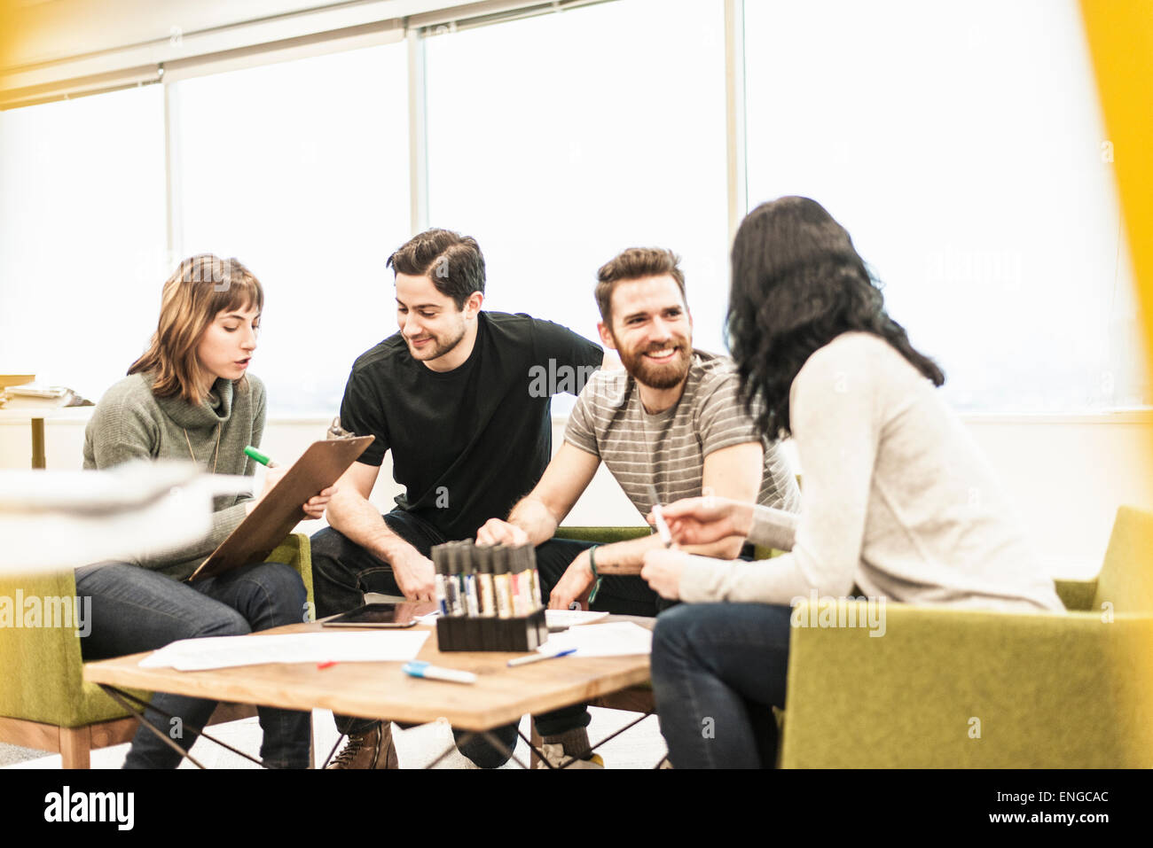 Vier Personen sitzen an einem Tisch mit Kollegen bei einer Planungsbesprechung holding Farbstiften und arbeiten auf Papier und Tabletten. Stockfoto