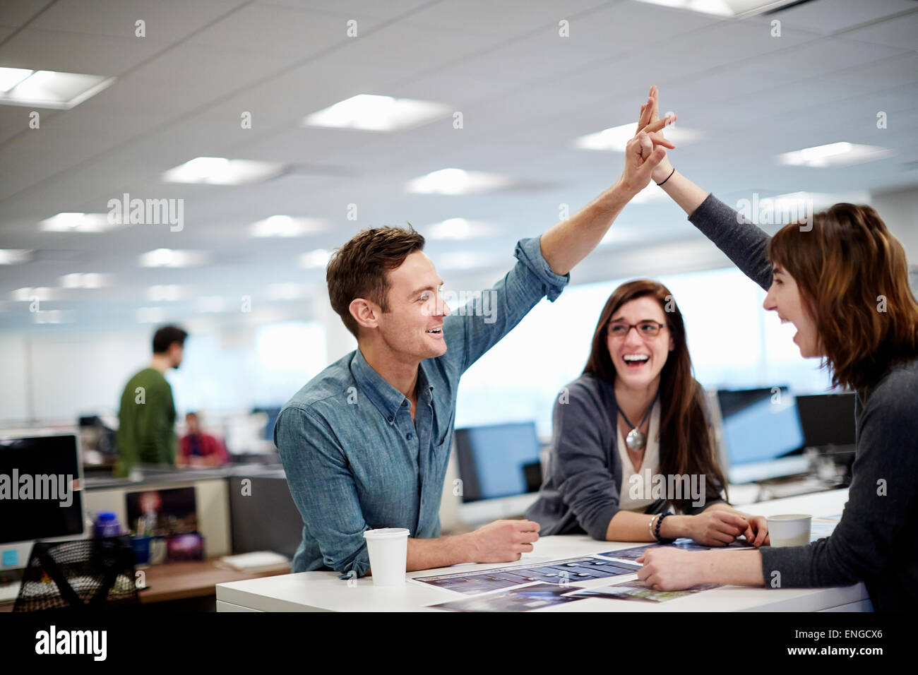 Drei Menschen in einem Büro mit Blick auf Fotografien und eine hohe fünf Geste. Stockfoto