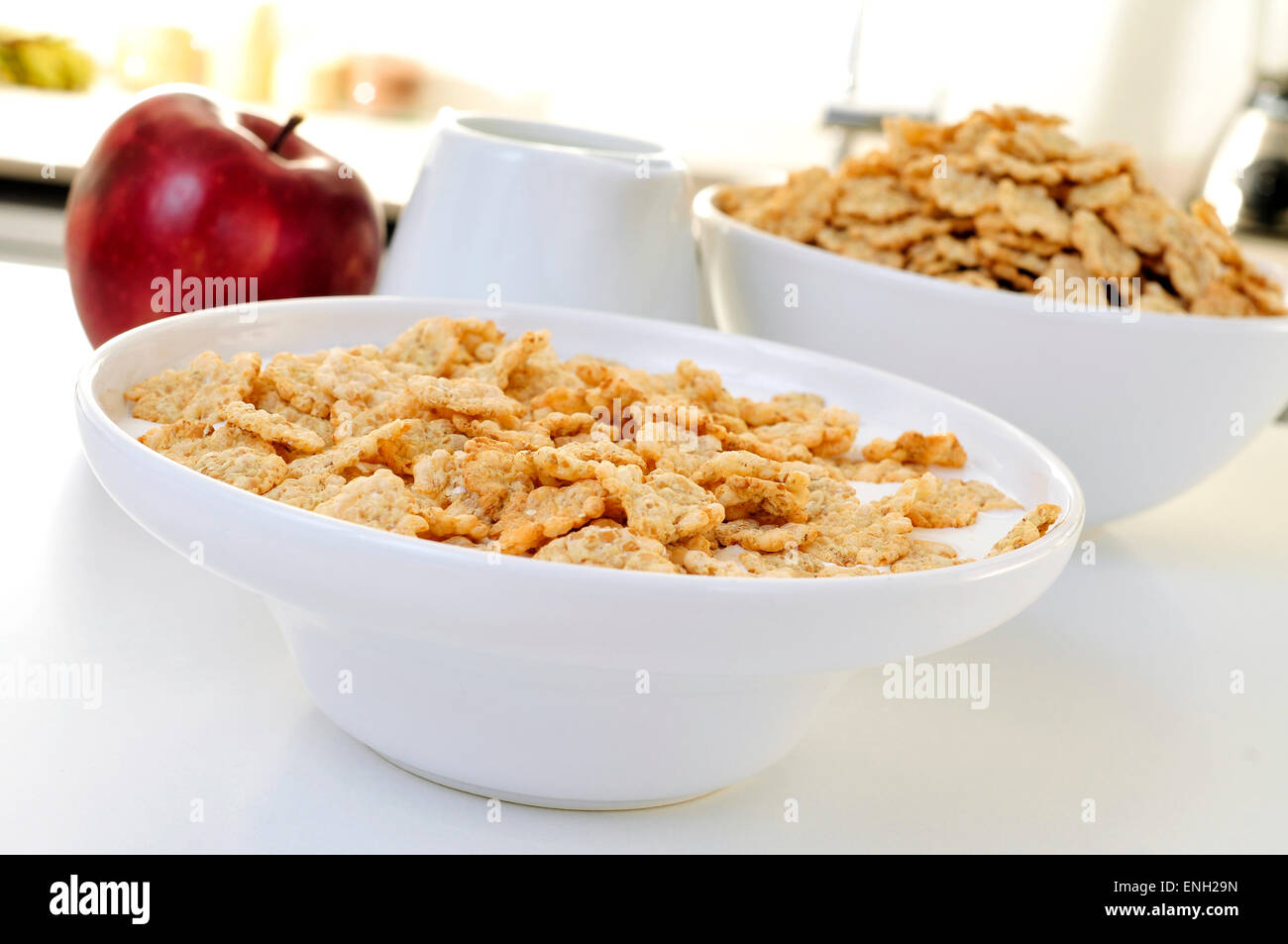 Nahaufnahme einer Schüssel mit Joghurt und Haferflocken Müsli zum Frühstück und ein roter Apfel auf dem Küchentisch Stockfoto