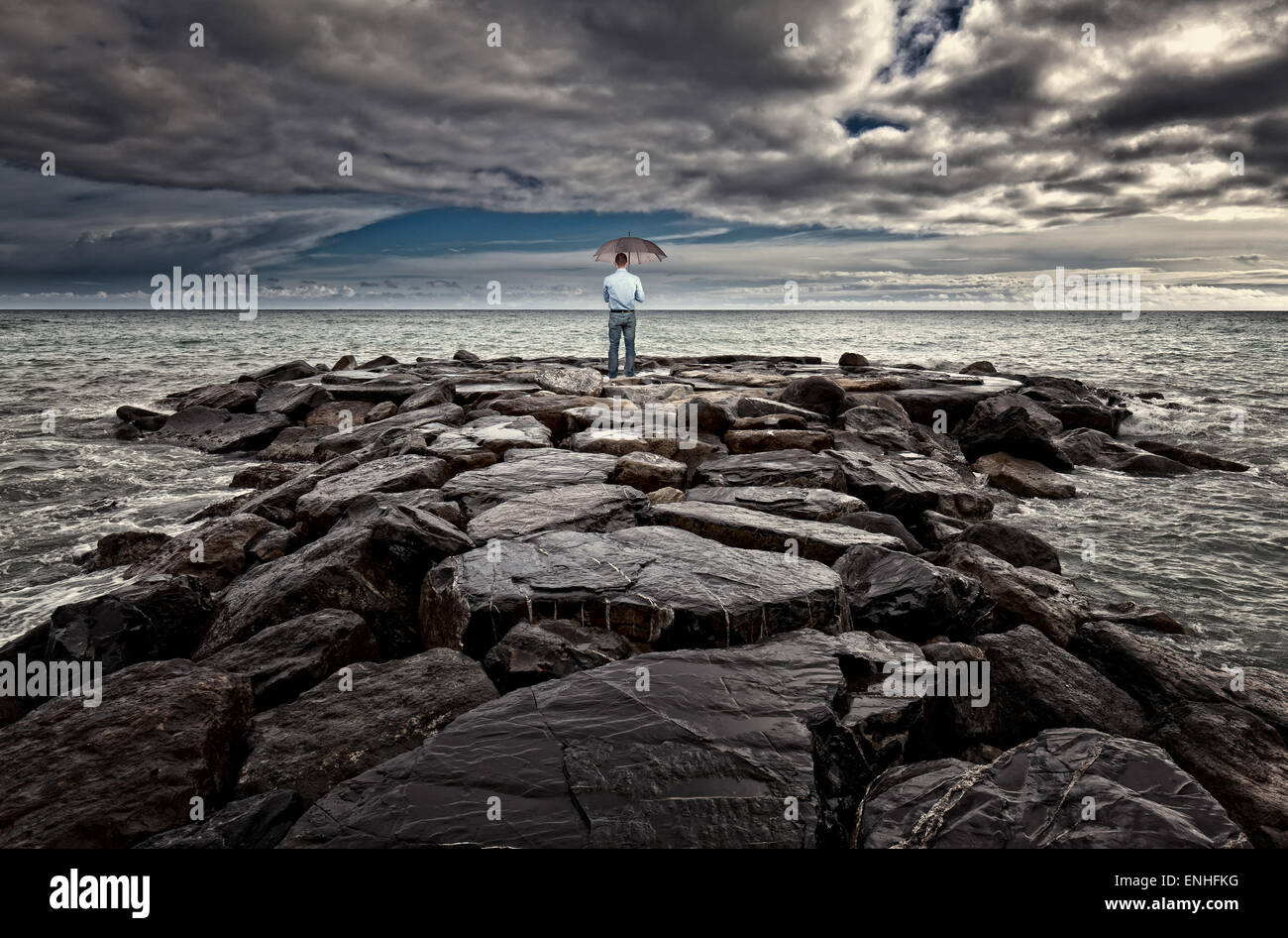 Mann mit Sonnenschirm am Meer Rock schlechtes Wetter Stockfoto