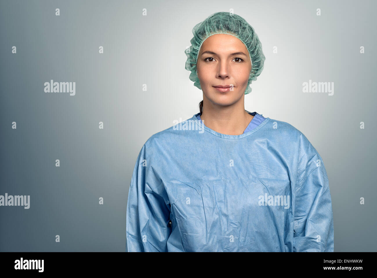 Attraktiven mittleren Alters Ärztin oder Krankenschwester in Peelings und eine Sterilität Kappe über grauen Hintergrund direkt in die Kamera schaut Stockfoto