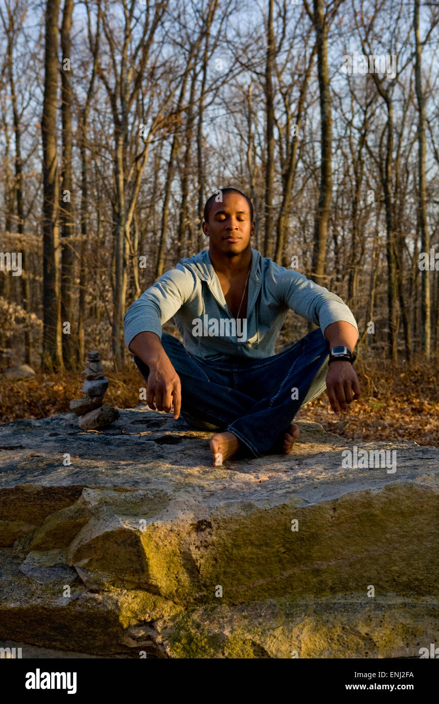 Afrikanische amerikanischer Mann meditiert auf einem Felsen im Wald Stockfoto