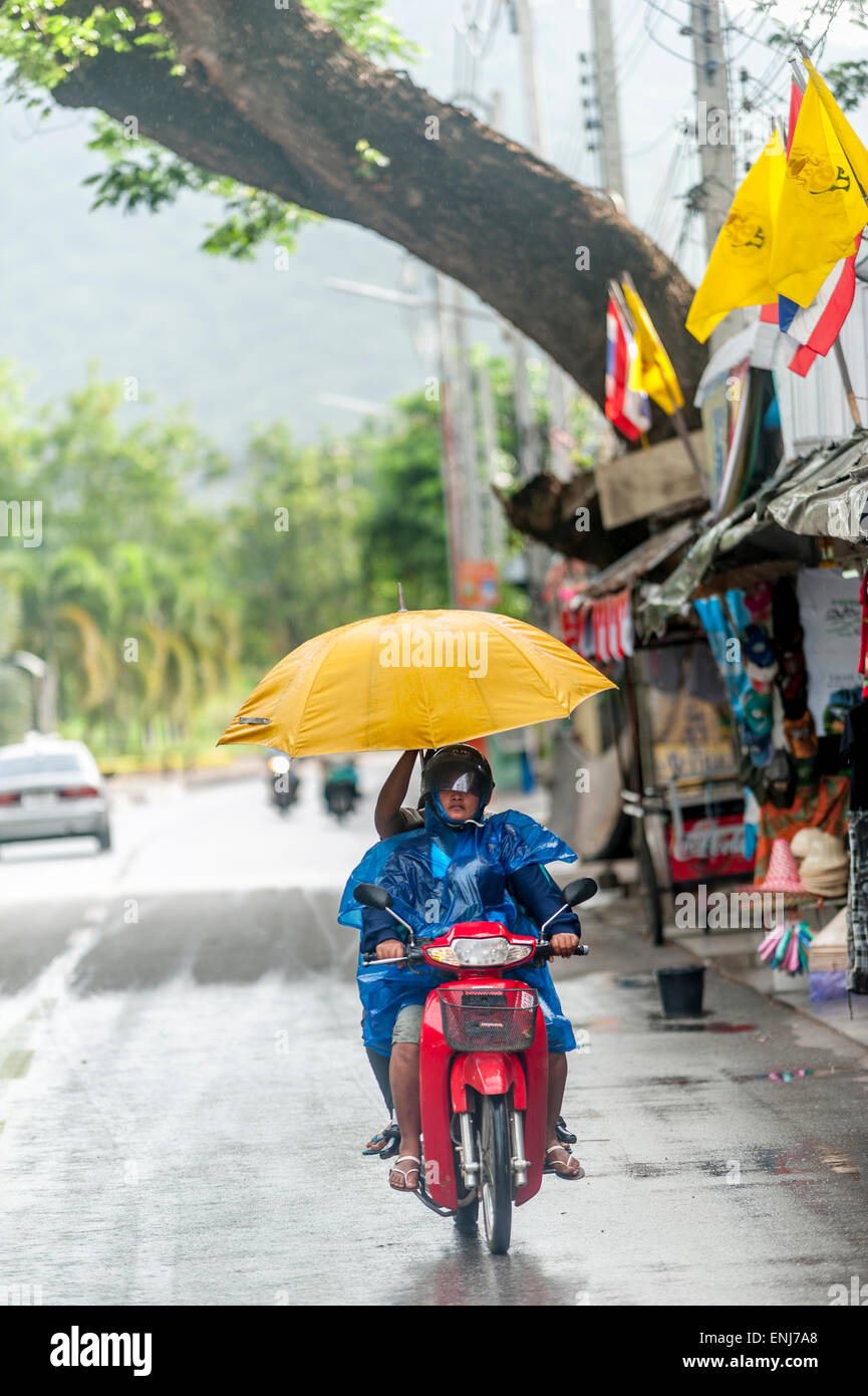 Koppeln Sie mit einem Regenschirm auf einem Motorrad im Regen. Kanchanaburi Provinz Kanchanaburi, Thailand Stockfoto
