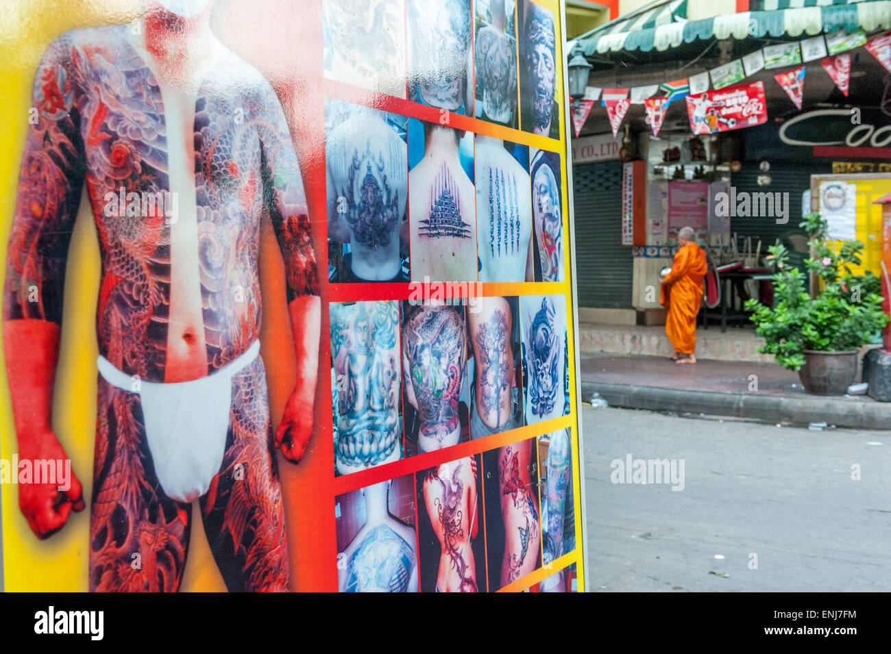 Buddhistischer Mönch auf seiner Morgen Almosen runden ein großes Display für ein Tattoo-Studio vorbei. Bangkok. Thailand Stockfoto