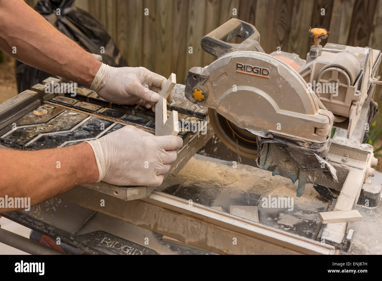 ARLINGTON, VIRGINIA, USA - Arbeiter mit Latex Handschuhen schneidet keramische Fliesen mit einem feuchten Fliesen sah. Stockfoto