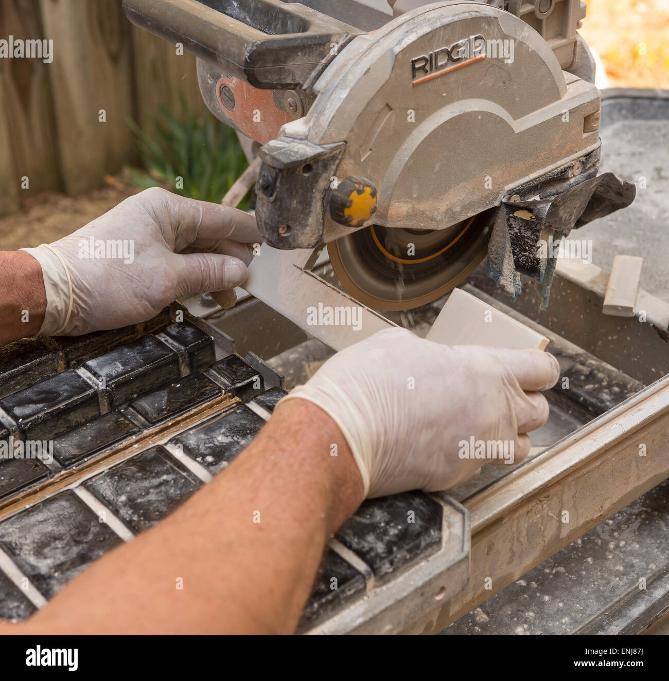 ARLINGTON, VIRGINIA, USA - Arbeiter mit Latex Handschuhen schneidet keramische Fliesen mit einem feuchten Fliesen sah. Stockfoto