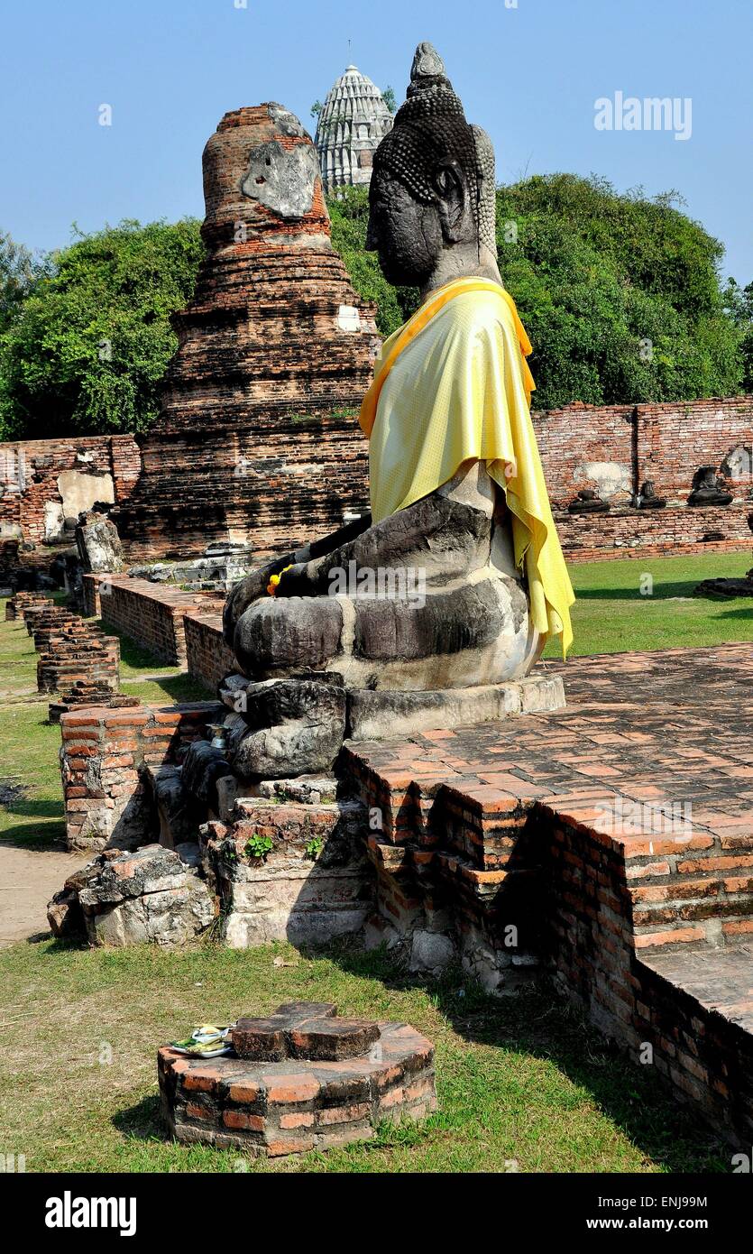 Ayutthaya, Thailand: Große Stein Buddha-Statue in einer gelben Schärpe Seide gehüllt sitzt inmitten der Ruinen am Royal Wat Mahathat Stockfoto