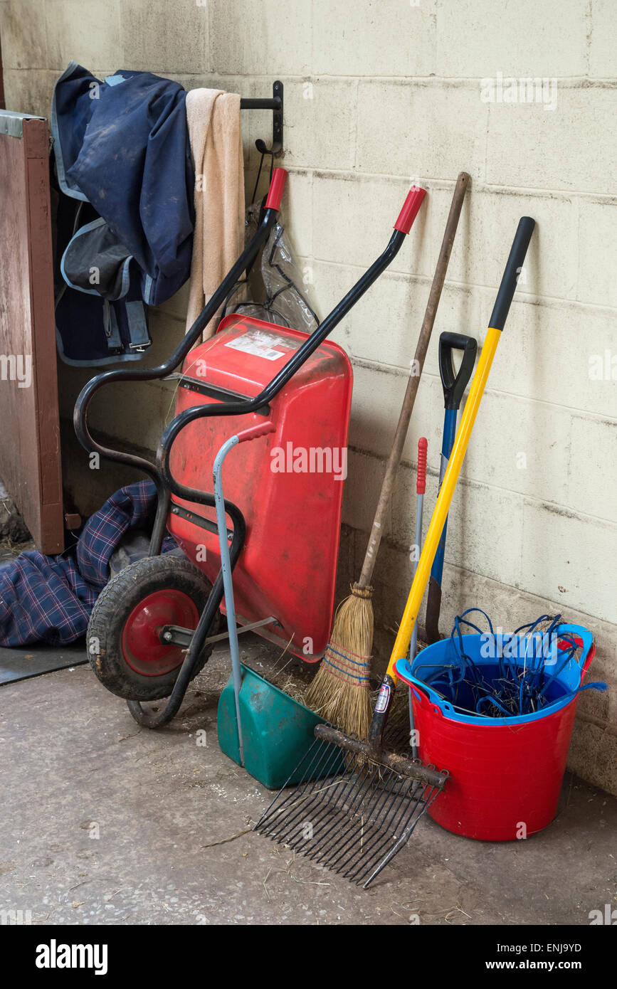 Schubkarre und andere Tools in einem Reitsport Stallhof. Eimer, Bürsten, Teppiche und Ausmisten Gabel. Stockfoto