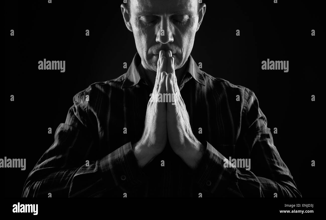 Vorderansicht eines Mannes beten im Dunkeln mit Licht auf beiden Seiten von ihm. Stockfoto