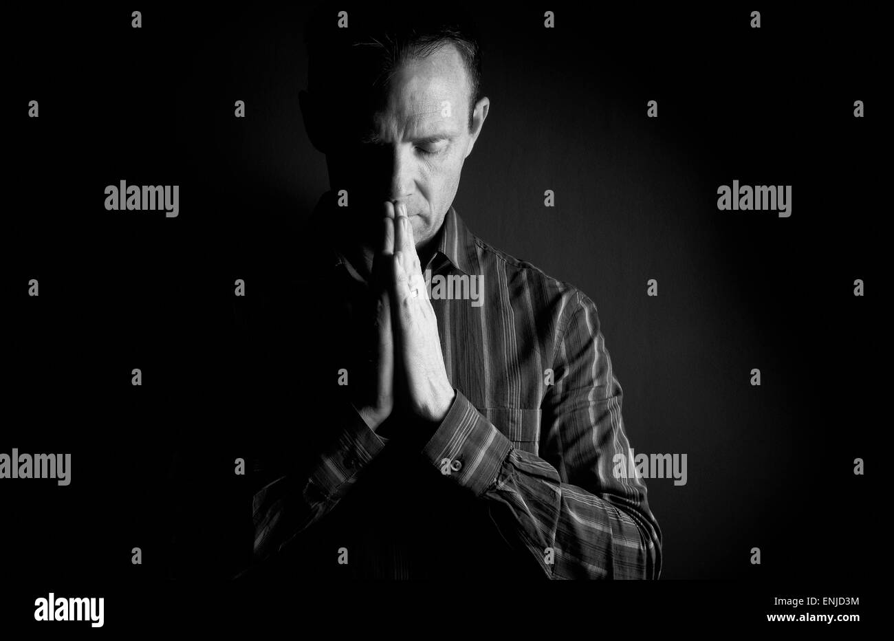 Vorderansicht eines Mannes beten im Dunkeln mit Licht an der Seite von ihm. Stockfoto