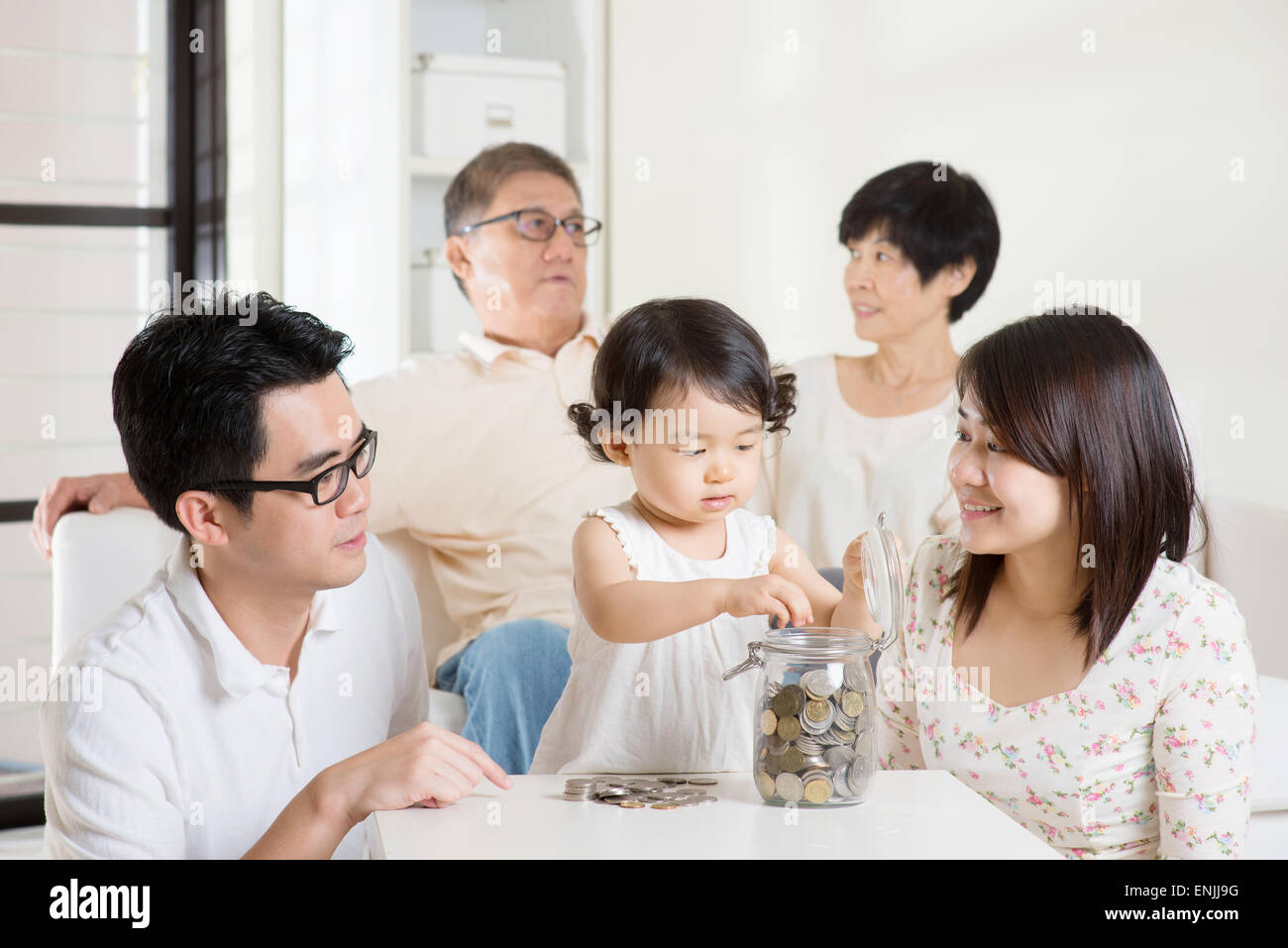 Kleinkind, Münzen in Geld Glas. Asiatische Familie Geld sparen Konzept. Multi-Generationen Lebensweise zu Hause. Stockfoto
