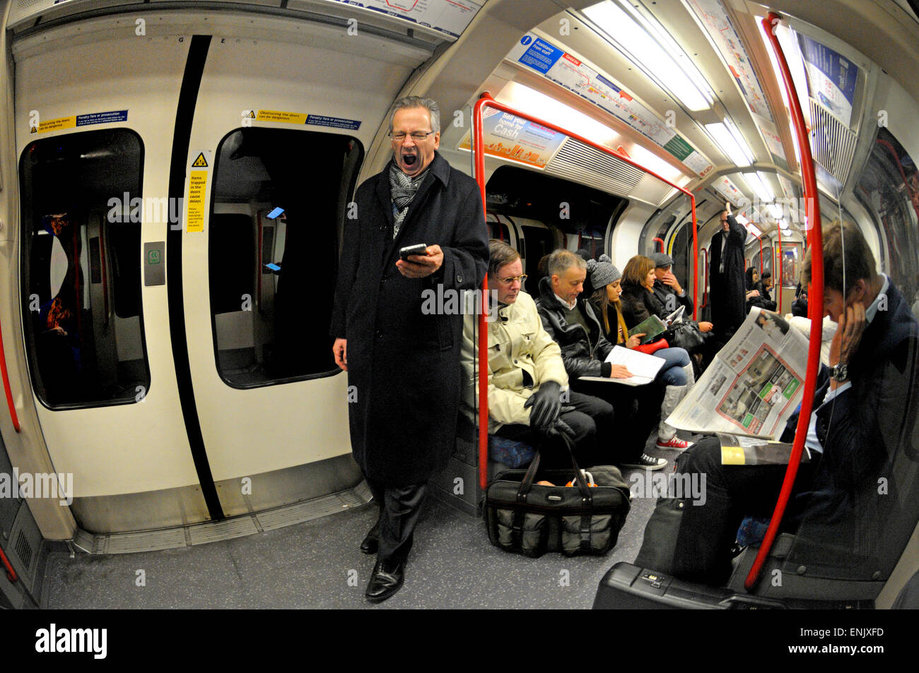 London, England, Vereinigtes Königreich. Londoner u-Bahn / Rohr. Mann mit Blick auf sein Handy und Gähnen Stockfoto