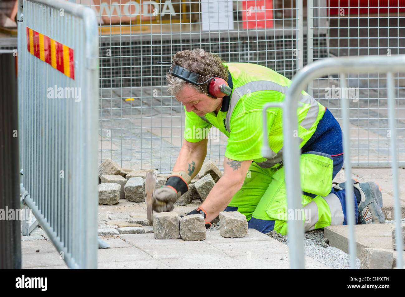 KARLSHAMN, Schweden - 6. Mai 2015: Unbekannte männliche Fertiger bei der Arbeit mit der Einstellung Granitsteine in öffentlichen Straße. Er arbeitet in einem eingezäunten Bereich außerhalb Geschäfte. Stockfoto