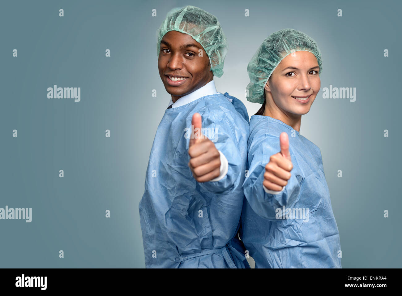 Hübscher junger afrikanischer Arzt oder Krankenpfleger in Scrubs und Sterilität Mütze schaut direkt in die Kamera über einen grauen Hintergrund, Stockfoto