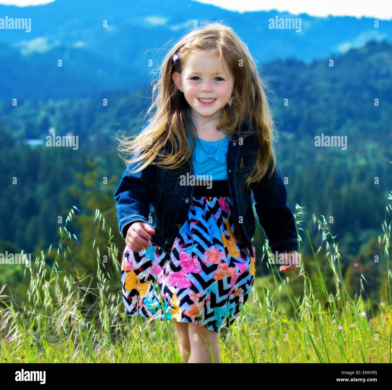 4 Jahre altes Mädchen mit den Bergen hinter ihr in einem leuchtend blauen Kleid. Stockfoto
