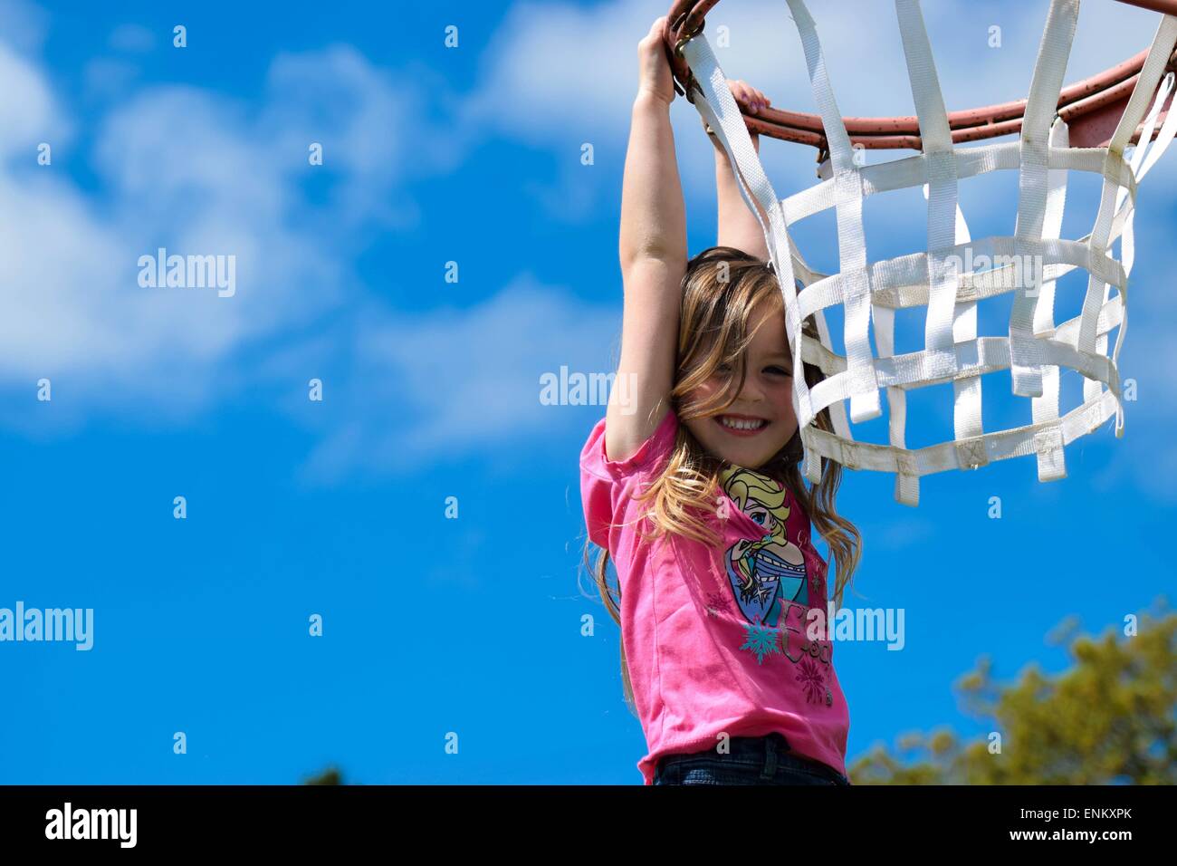 4 Jahre altes Mädchen hängt ein Basketballkorb mit dem Himmel hinter ihr. Stockfoto