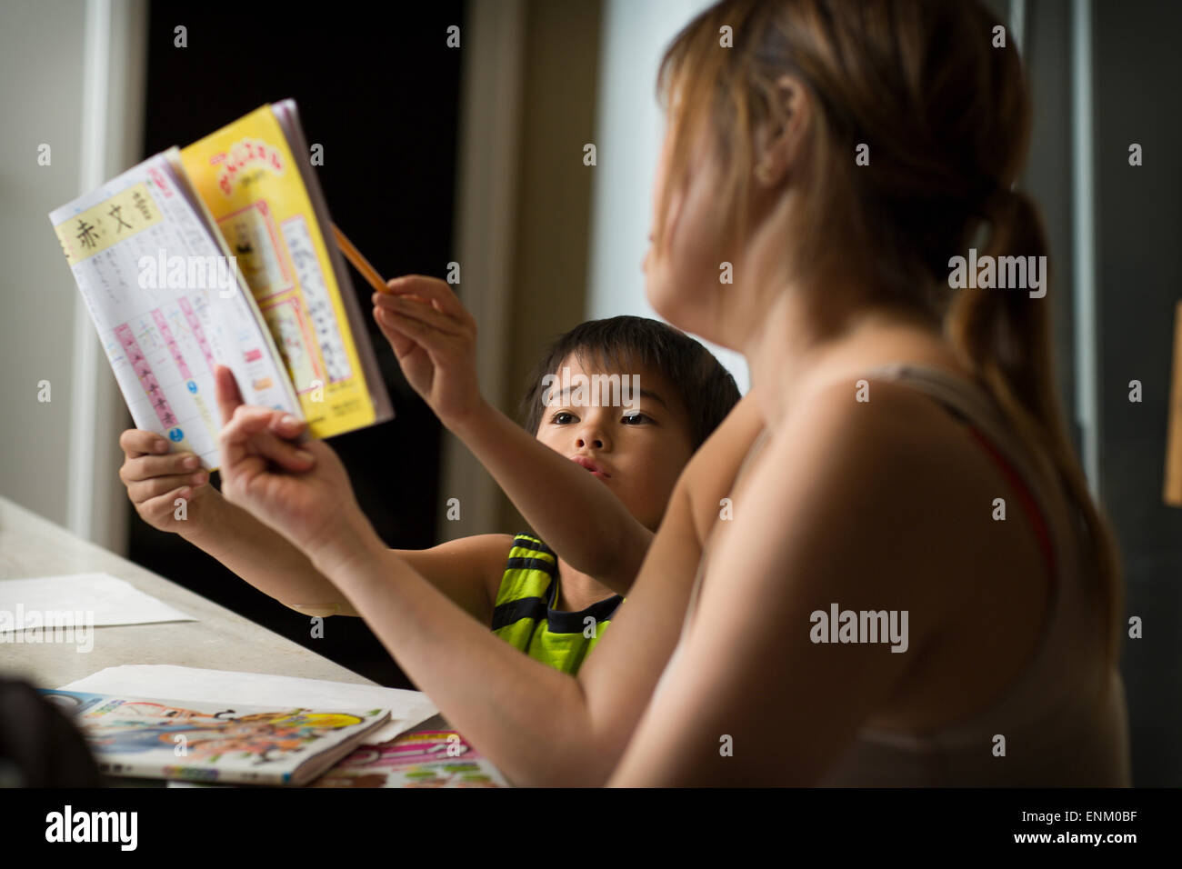 Ein japanischen Jungen studiert Japanische Hausaufgaben in der Küche, als seine Mutter ihm hilft. Stockfoto