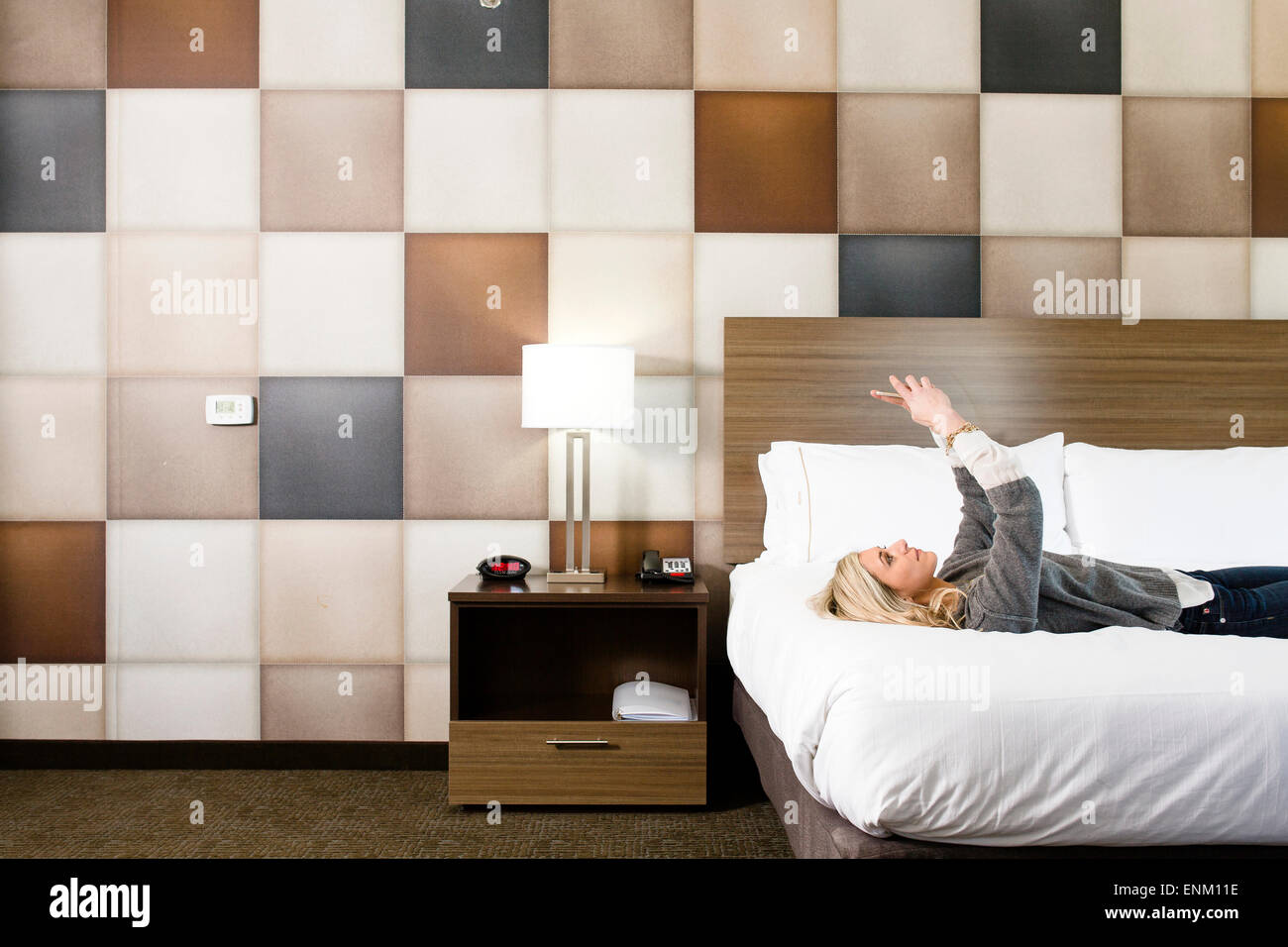 Eine schöne Dame nimmt Selfie, wie sie auf ein Motel Zimmer Bett liegt. Stockfoto