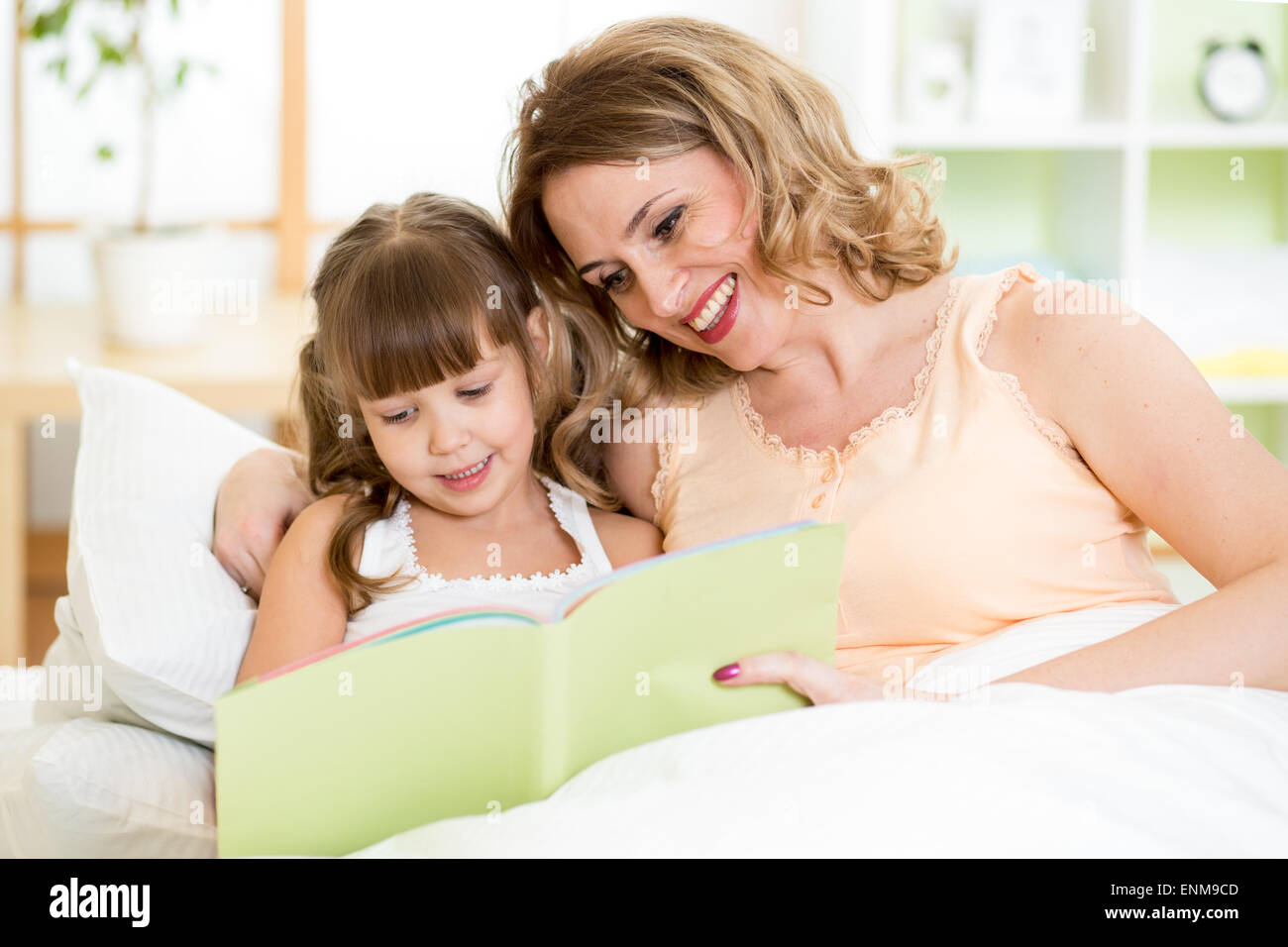 Glückliche Mutter und Tochter lesen ein Buch zusammen im Bett Stockfoto