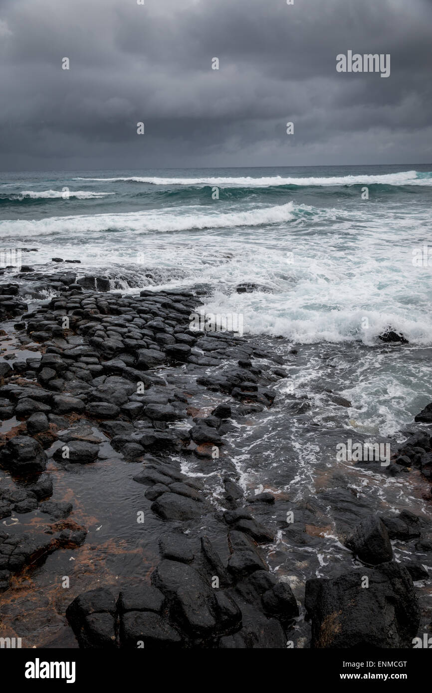 stürmischen Ozean, dramatischer Himmel. Ein Sturm sendet Wellen über einem felsigen vulkanischen Strand in Hawaii. Stockfoto