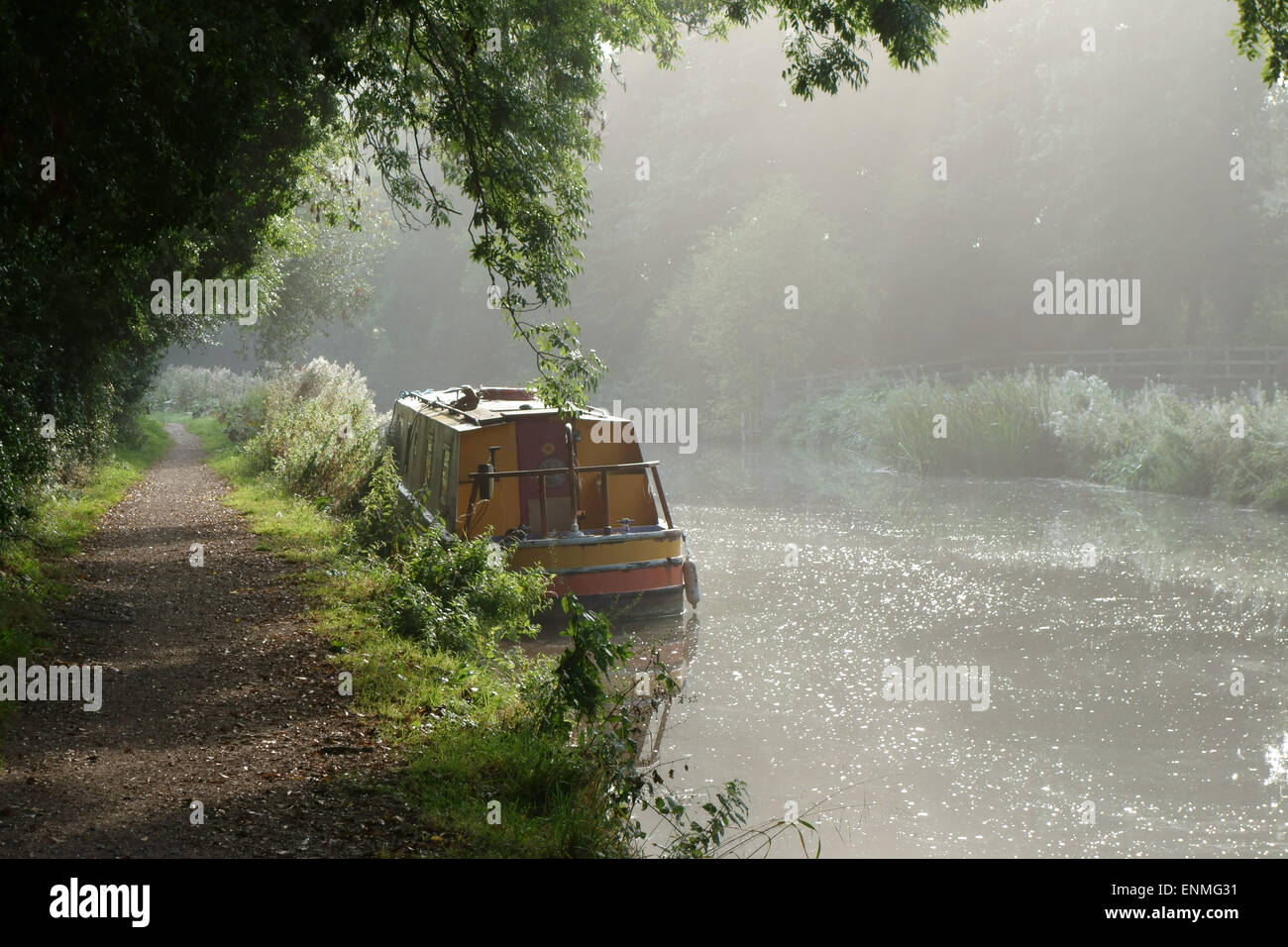 Leinpfad und einem schmalen Boot vertäut am Ufer des Kennet & Avon Canal an einem hellen nebligen Spätsommer-Morgen in der Nähe von Bäumen Stockfoto