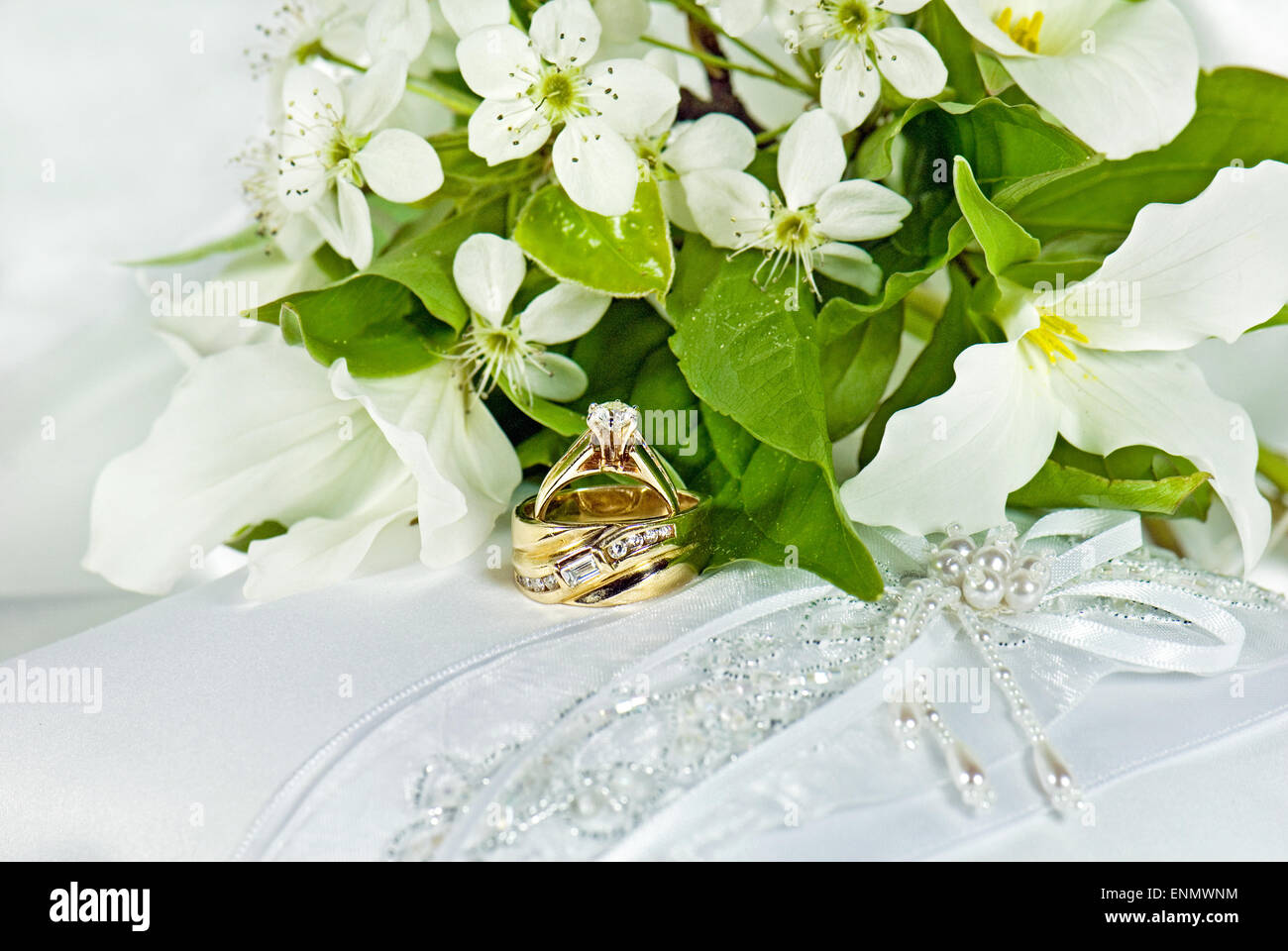 Trauringe mit Trillium Brautstrauß auf einem weißen satin Kissen. Stockfoto