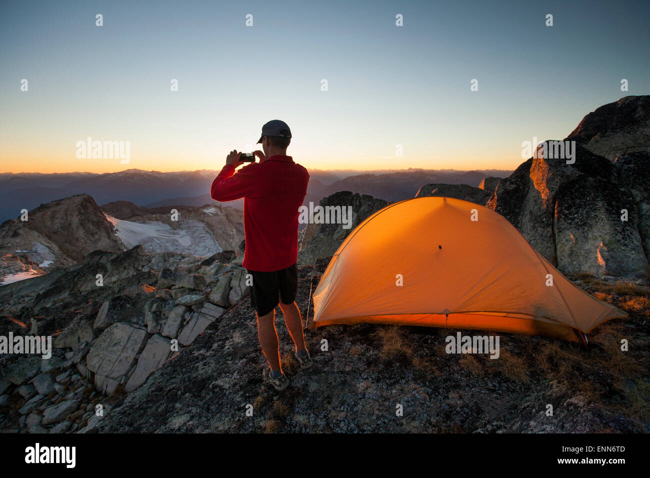 Ein Wanderer nimmt ein Bild des Sonnenuntergangs mit seinem Smartphone beim Zelten auf dem Gipfel des Steinbrech. Stockfoto