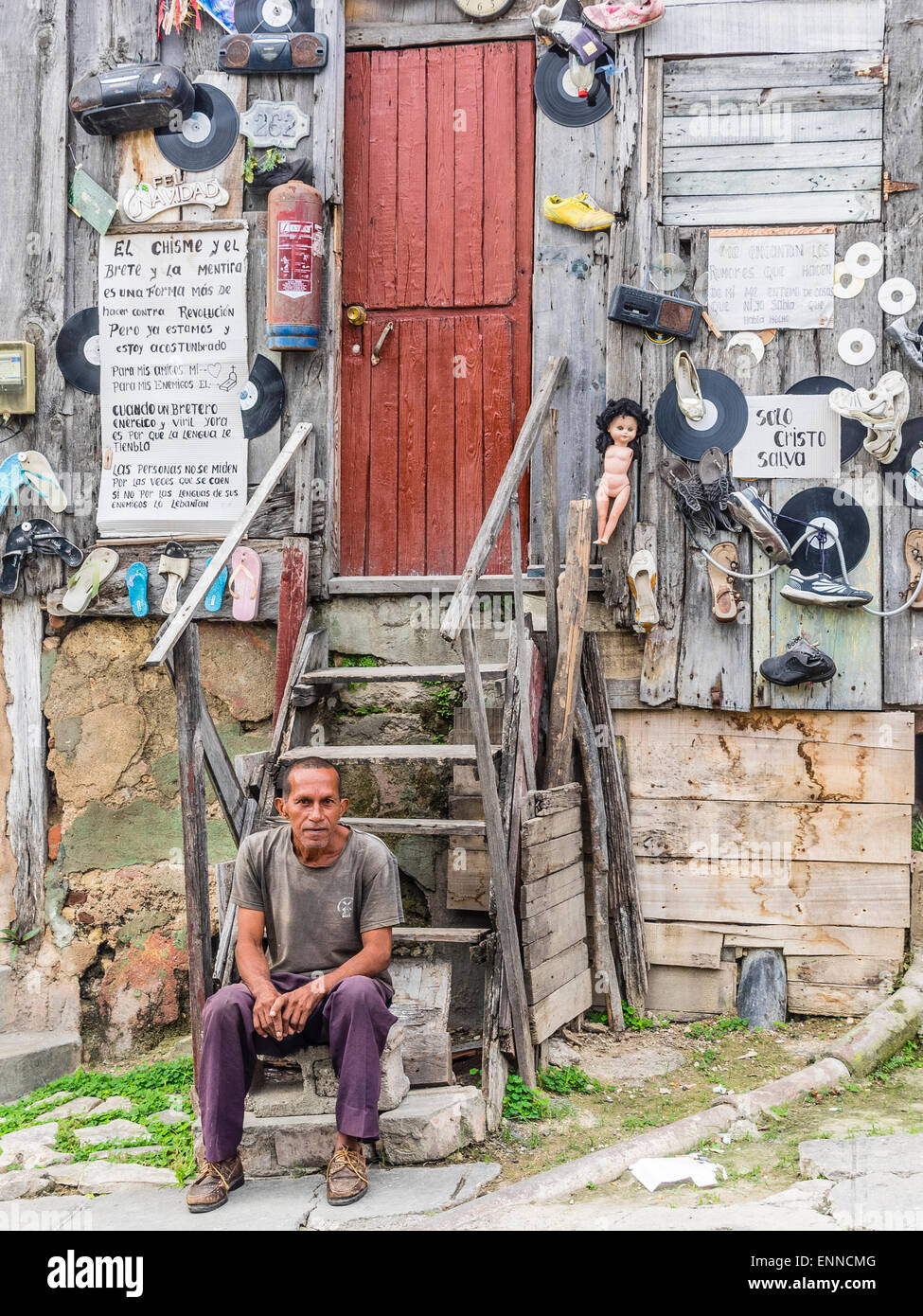 Ein Hispanic kubanischen sitzt Man auf den Stufen von seinem sehr seltsam, eingerichtete unkonventionell Holzhaus. Stockfoto