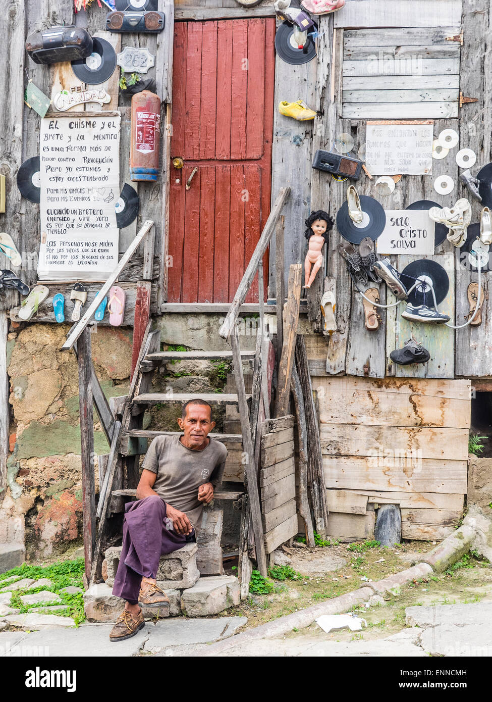 Ein Hispanic kubanischen sitzt Man auf den Stufen von seinem sehr seltsam, eingerichtete unkonventionell Holzhaus. Stockfoto