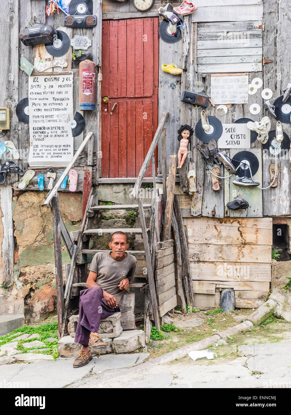 Ein Hispanic kubanischen sitzt Man auf den Stufen von seinem sehr seltsam, eingerichtete unkonventionell Holzhaus. Stockfoto