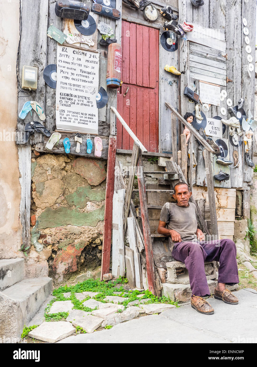 Ein Hispanic kubanischen sitzt Man auf den Stufen von seinem sehr seltsam, eingerichtete unkonventionell Holzhaus. Stockfoto