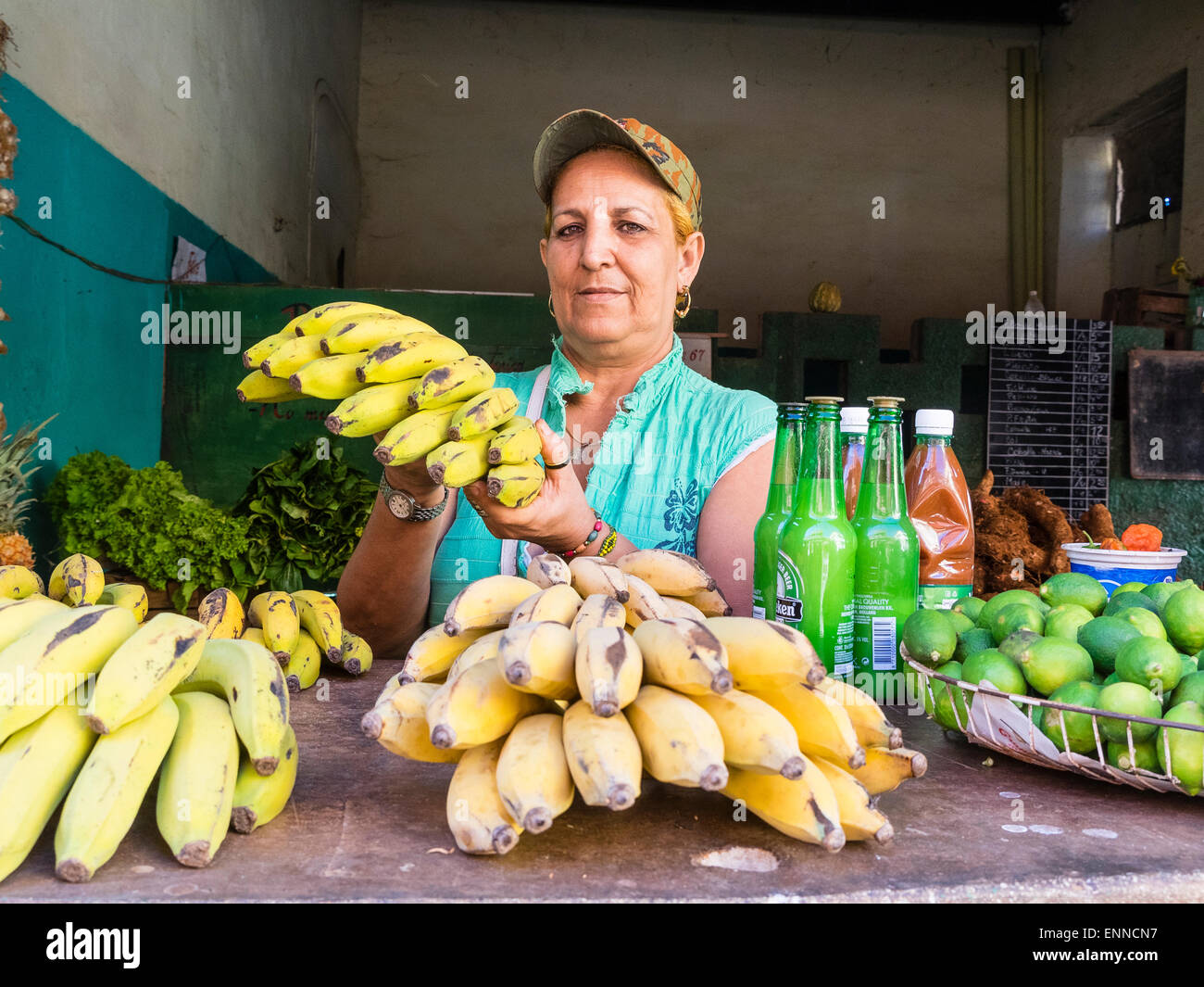 Eine weibliche kubanischen Produkten stehen Verkäufer trägt eine Baseballkappe und hält ein Bündel Bananen beim Blick geradeaus. Stockfoto