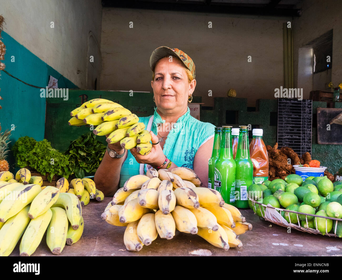 Eine weibliche kubanischen Produkten stehen Verkäufer trägt eine Baseballkappe und hält ein Bündel Bananen beim Blick geradeaus. Stockfoto
