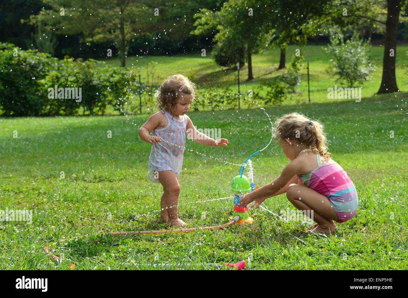 Zwei junge Mädchen, ein Kleinkind und ein Pre-Schooler, spielen mit einem Spielzeug Wasser Sprinkler.  Wasser rund um die Mädchen spritzen Stockfoto