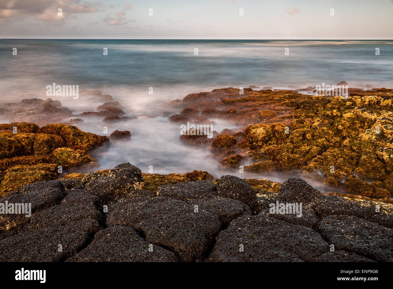 Eine Langzeitbelichtung der Wellen Waschen über vulkanische Felsen an einem tropischen Strand. Stockfoto