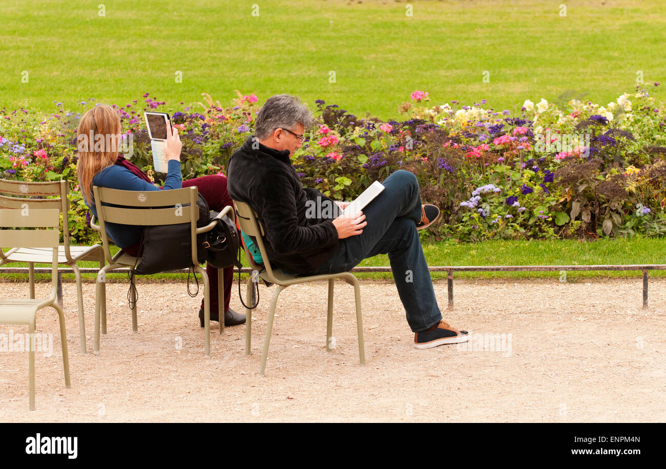 Paar-Lesung mit ihren Tabletten, Entspannung im Jardin du Luxembourg. Stockfoto