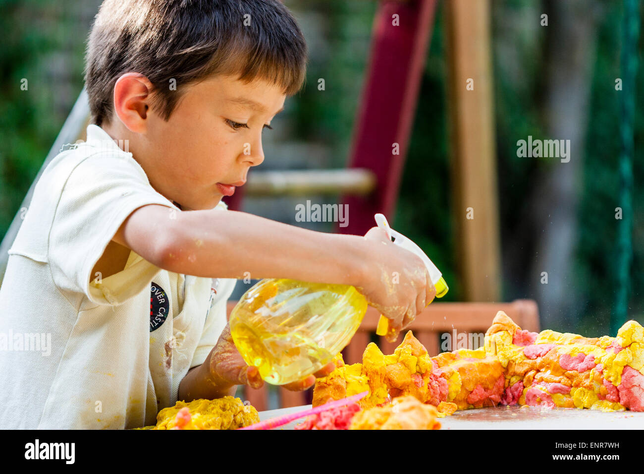 Nahaufnahme, von einem gemischten Rassenkind, Junge, asiatisch-kaukasischen, 7-8 Jahre alt, spielt im Freien, benetzt Spielteig auf einem Tisch mit einem Wasserspray. Stockfoto
