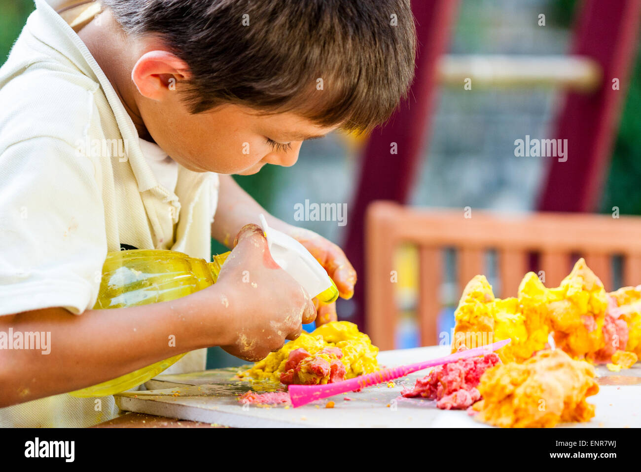 Nahaufnahme, von einem gemischten Rassenkind, Junge, asiatisch-kaukasischen, 7-8 Jahre alt, spielt im Freien, benetzt Spielteig auf einem Tisch mit einem Wasserspray. Stockfoto