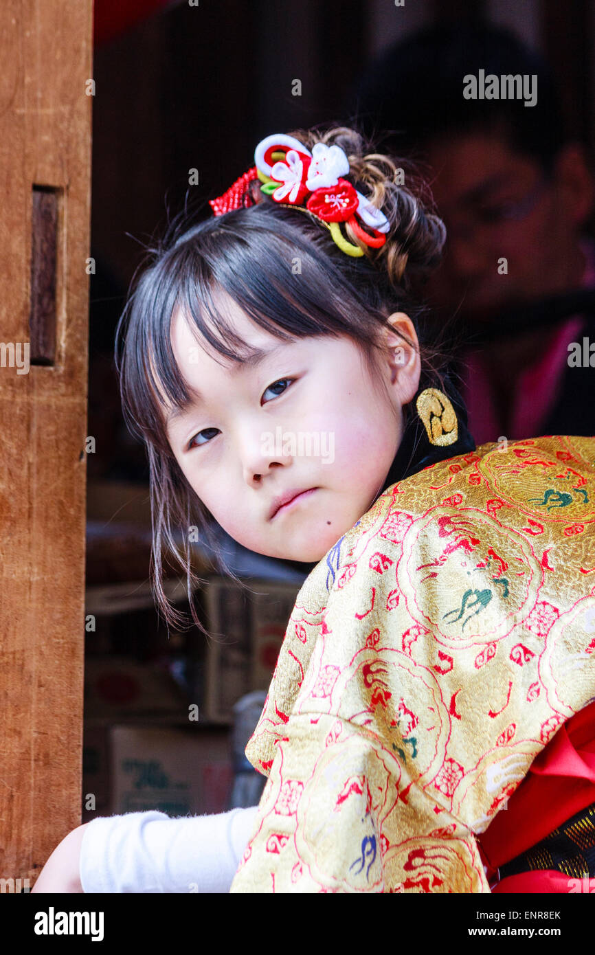 Japanisches Kind, Mädchen, 7-8 Jahre alt, in traditioneller Tracht, Kimono gekleidet, und sitzend in einem Yama-Wagen auf einem Festival, drehte sich um, um den Betrachter zu betrachten. Stockfoto