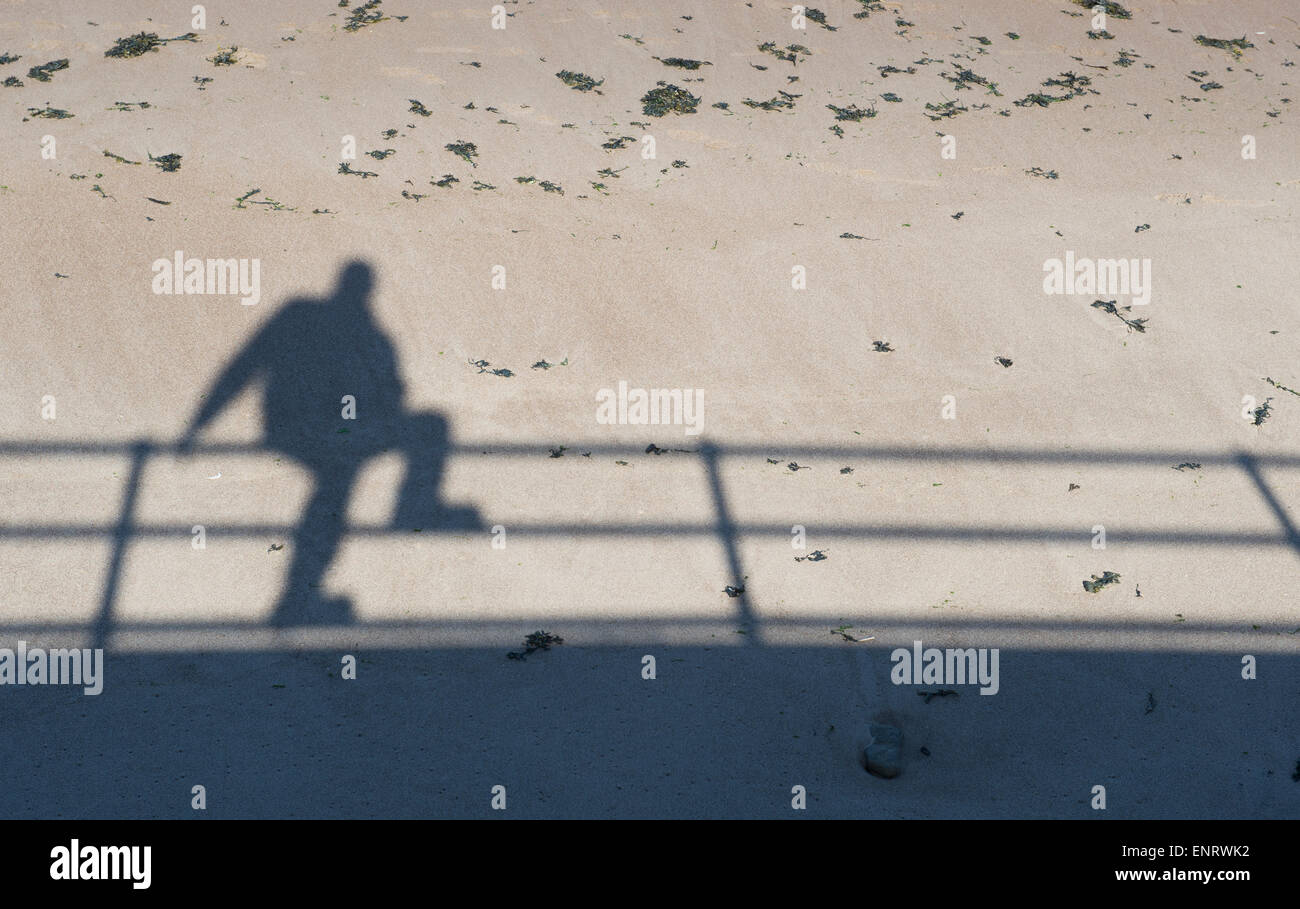 Schatten eines Mannes saß auf einem Geländer Promenade am Strand. UK Stockfoto