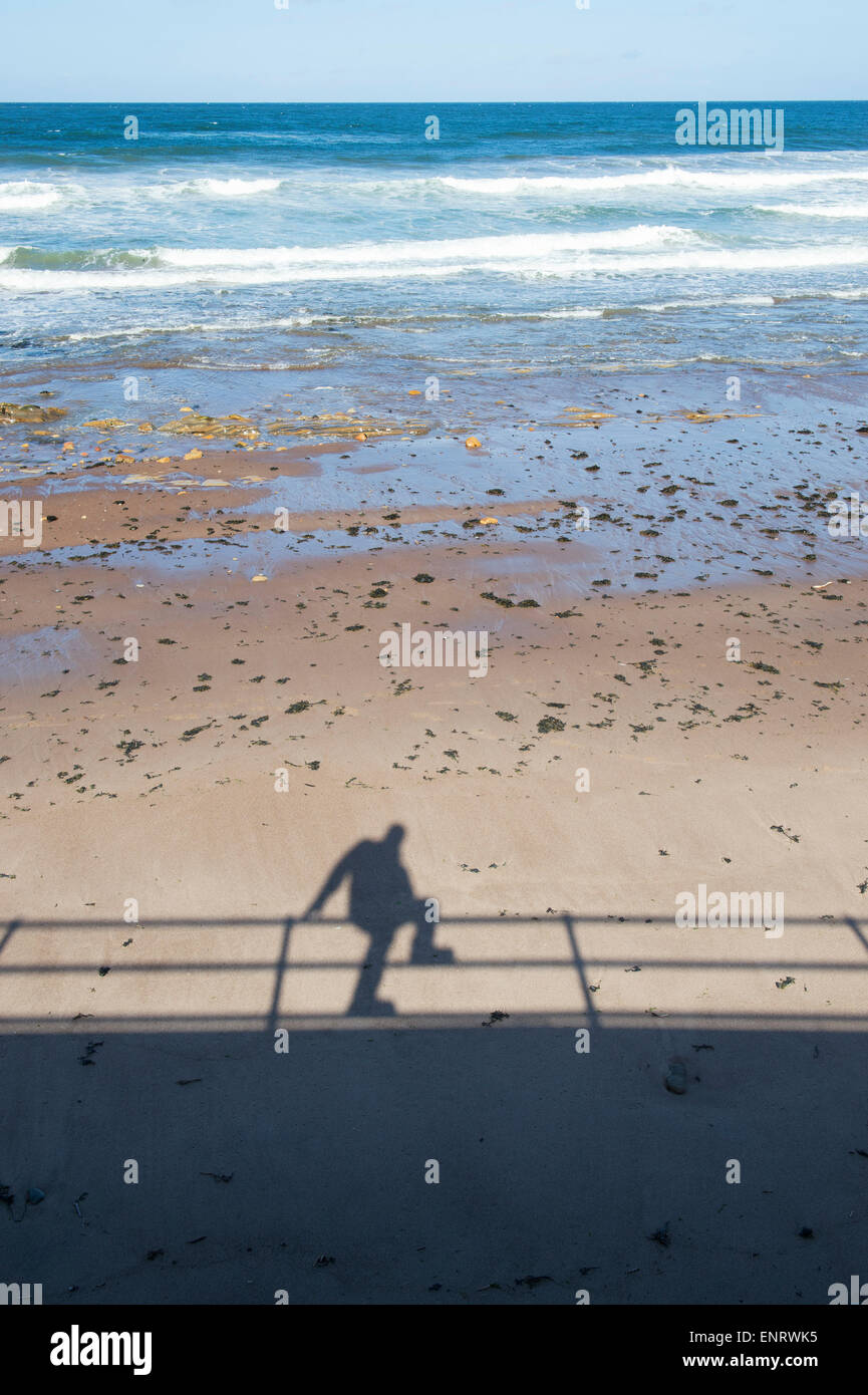 Schatten eines Mannes saß auf einem Geländer Promenade am Strand. UK Stockfoto