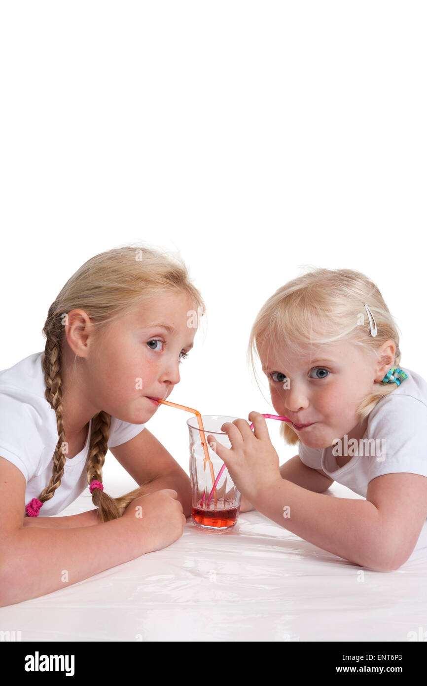 Porträt von zwei blonden Schwestern trinken rote Limonade mit einem Strohhalm auf weißem Hintergrund Stockfoto