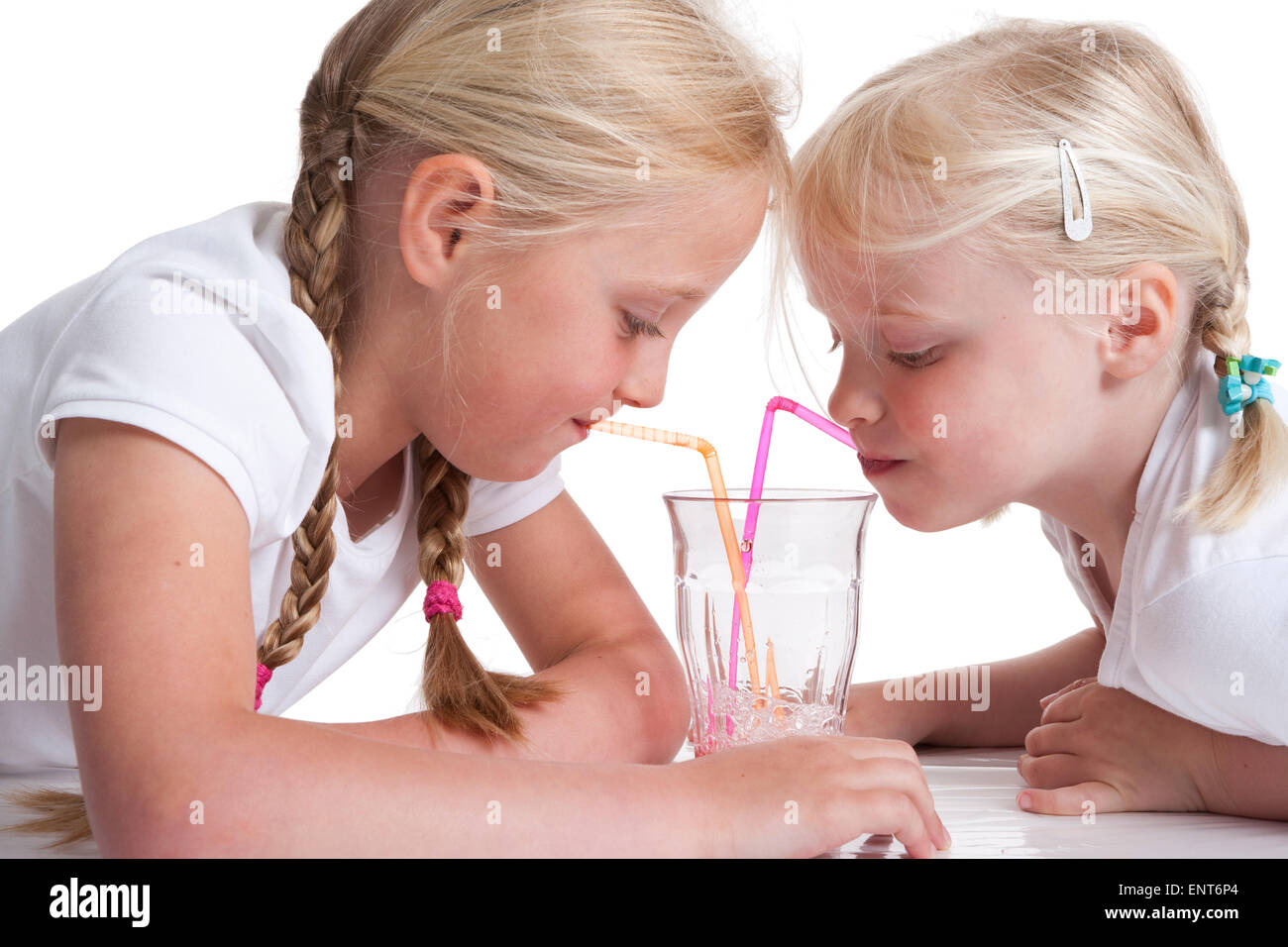 Porträt von zwei blonden Schwestern trinken Limonade mit einem Strohhalm auf weißem Hintergrund Stockfoto